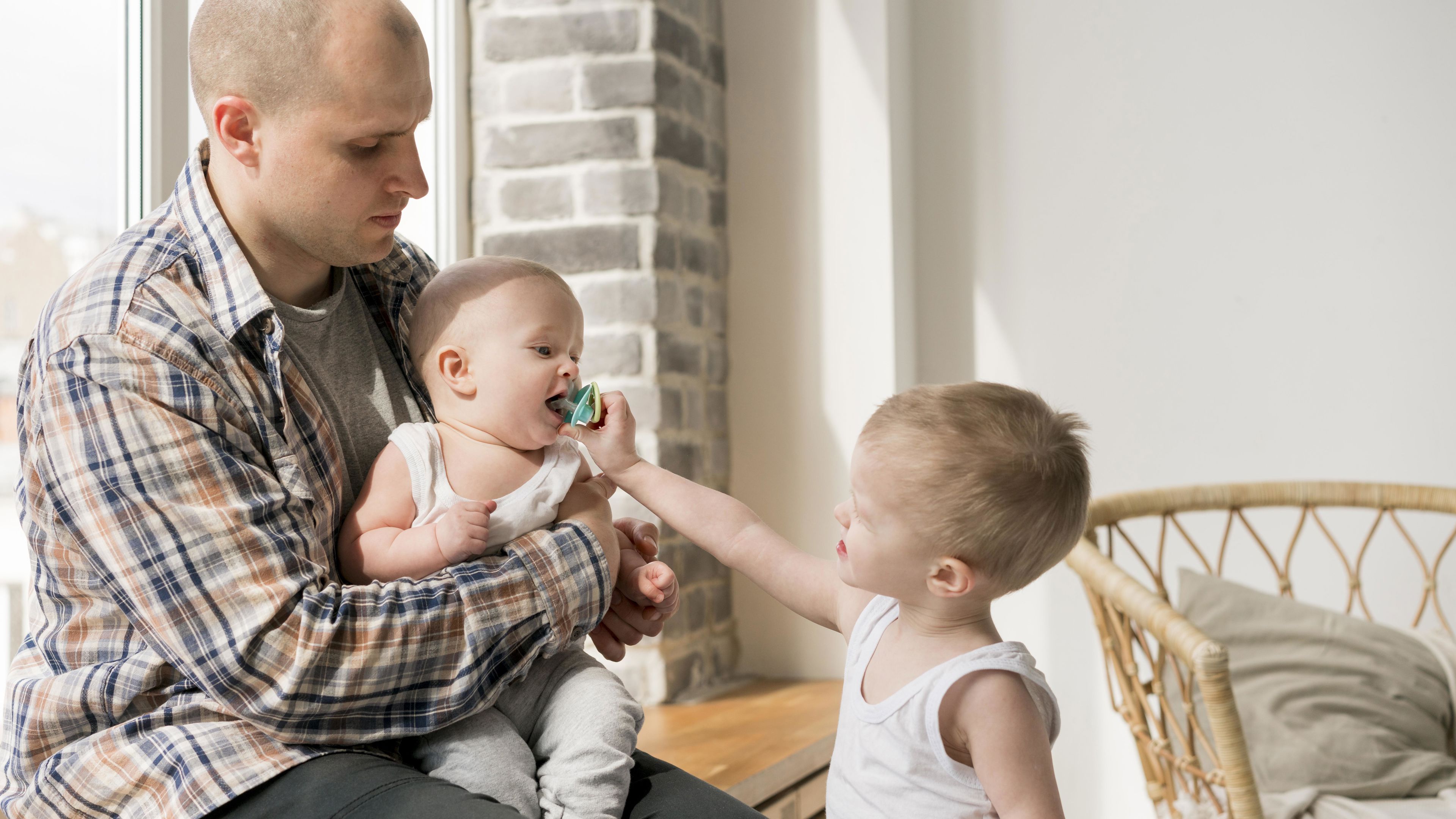 Stående dreng giver baby, der sidder hos far, sut i munden