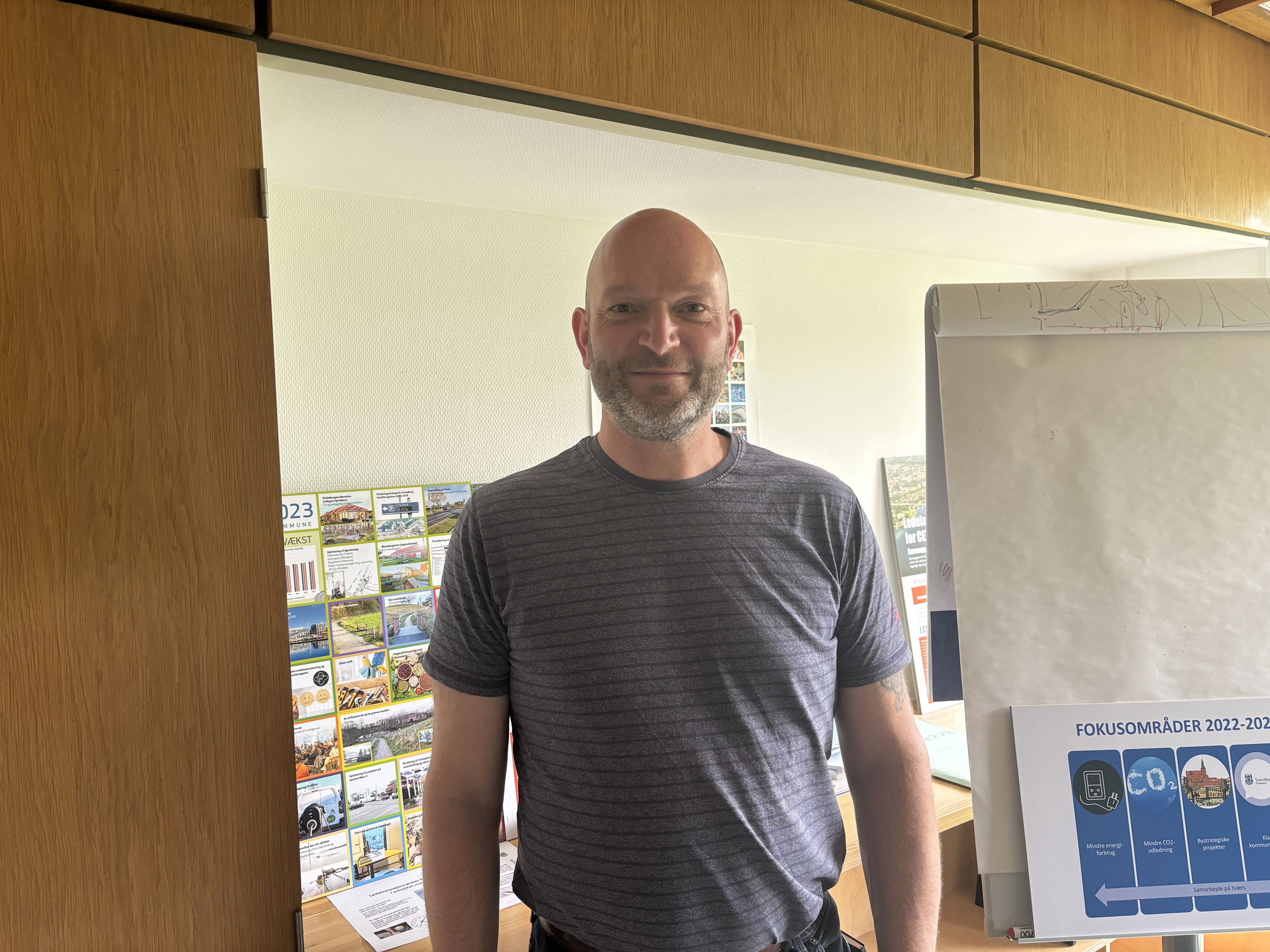 Midaldrende mand med skæg, som står foran brochurer og flipover