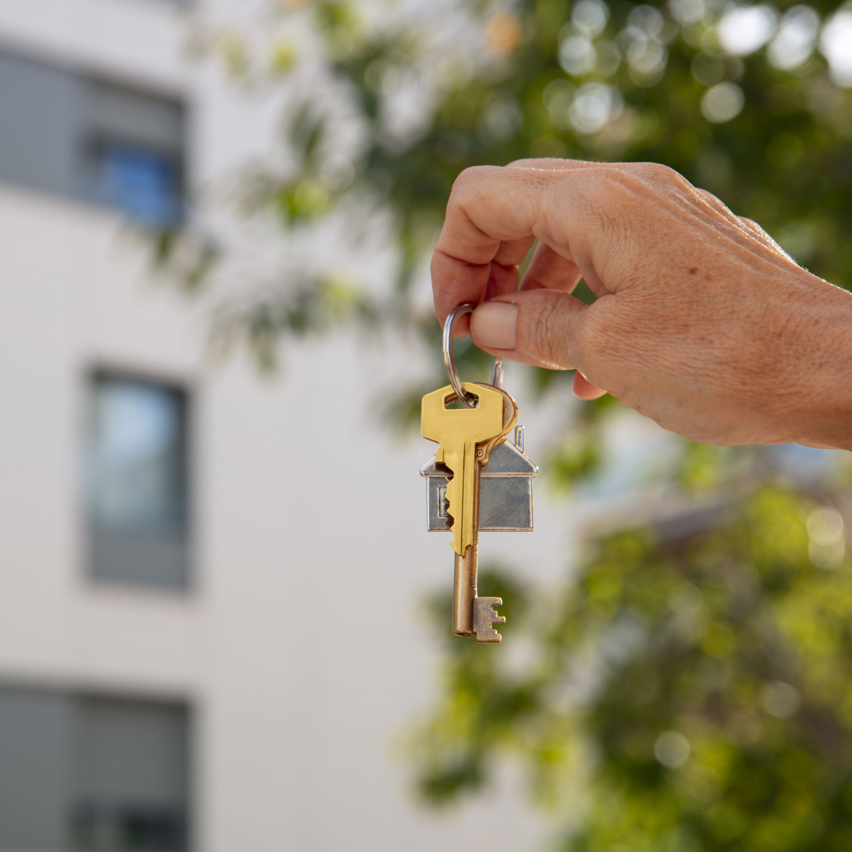 Hånd holder husnøgler. Et hus ses sløret i baggrunden