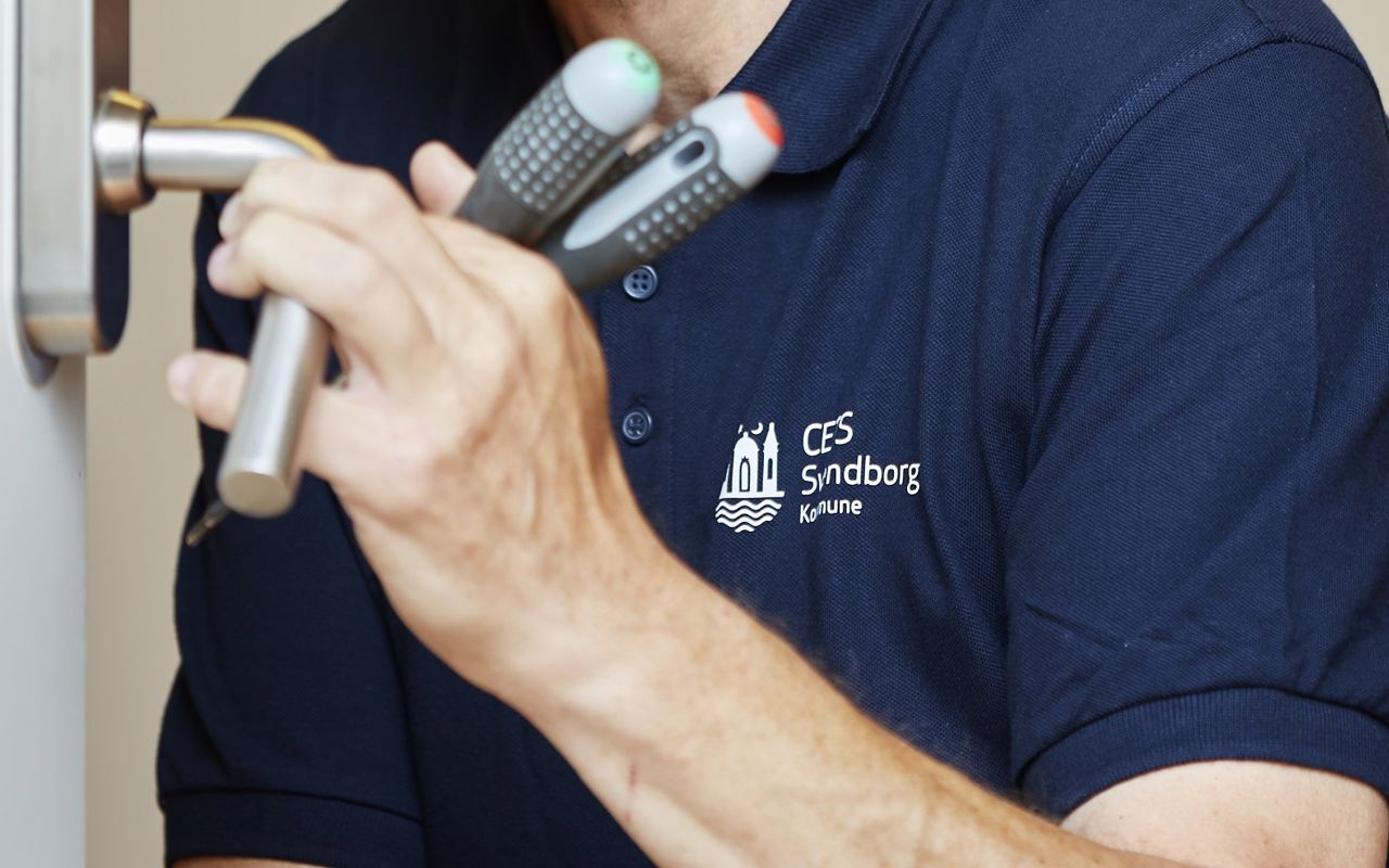 Hænder med værktøj som holder om et dørhåndtag.