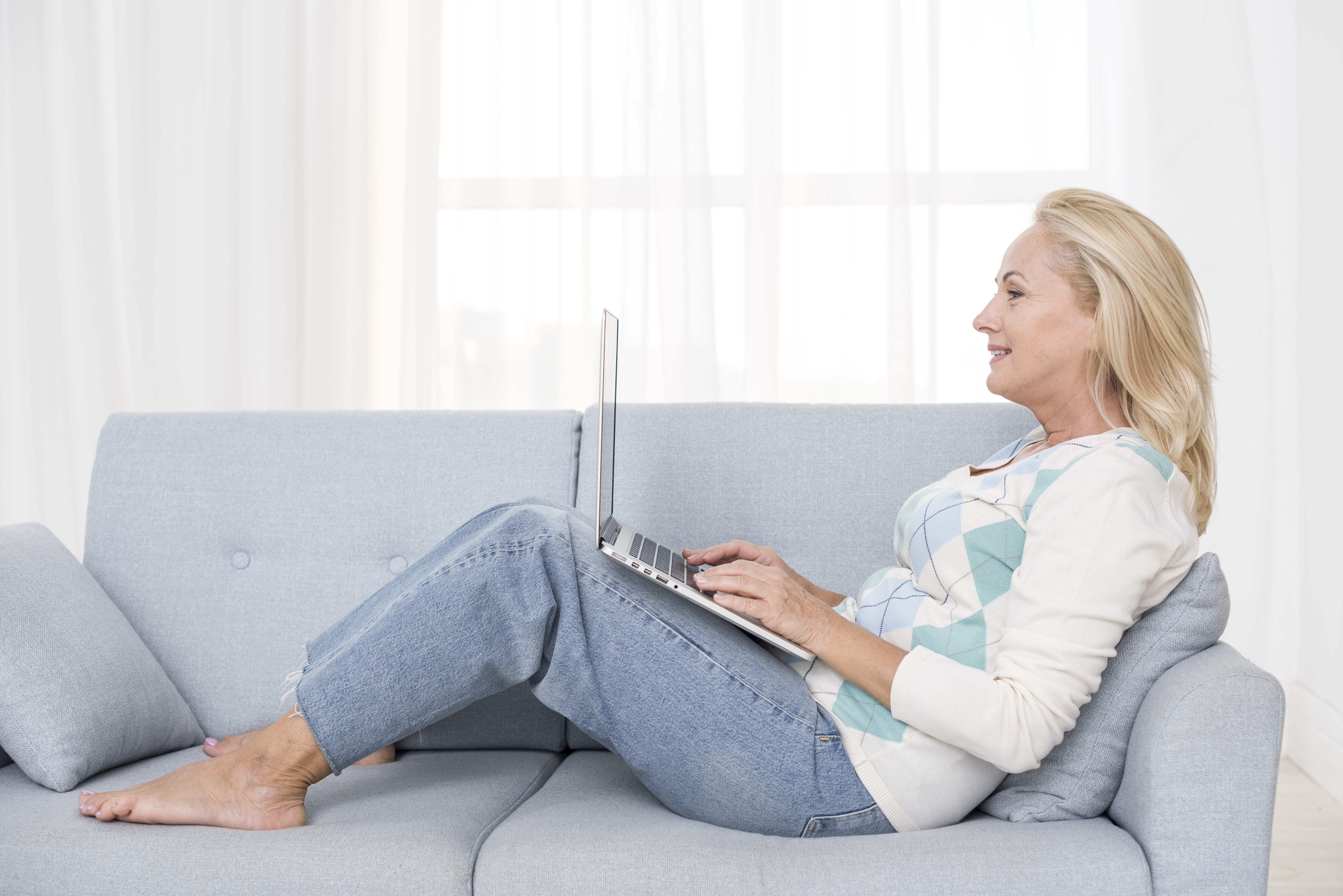 Dame, der sidder på sofa med opslået pc på lårene