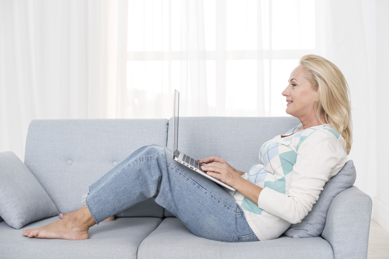 Dame, der sidder på sofa med opslået pc på lårene