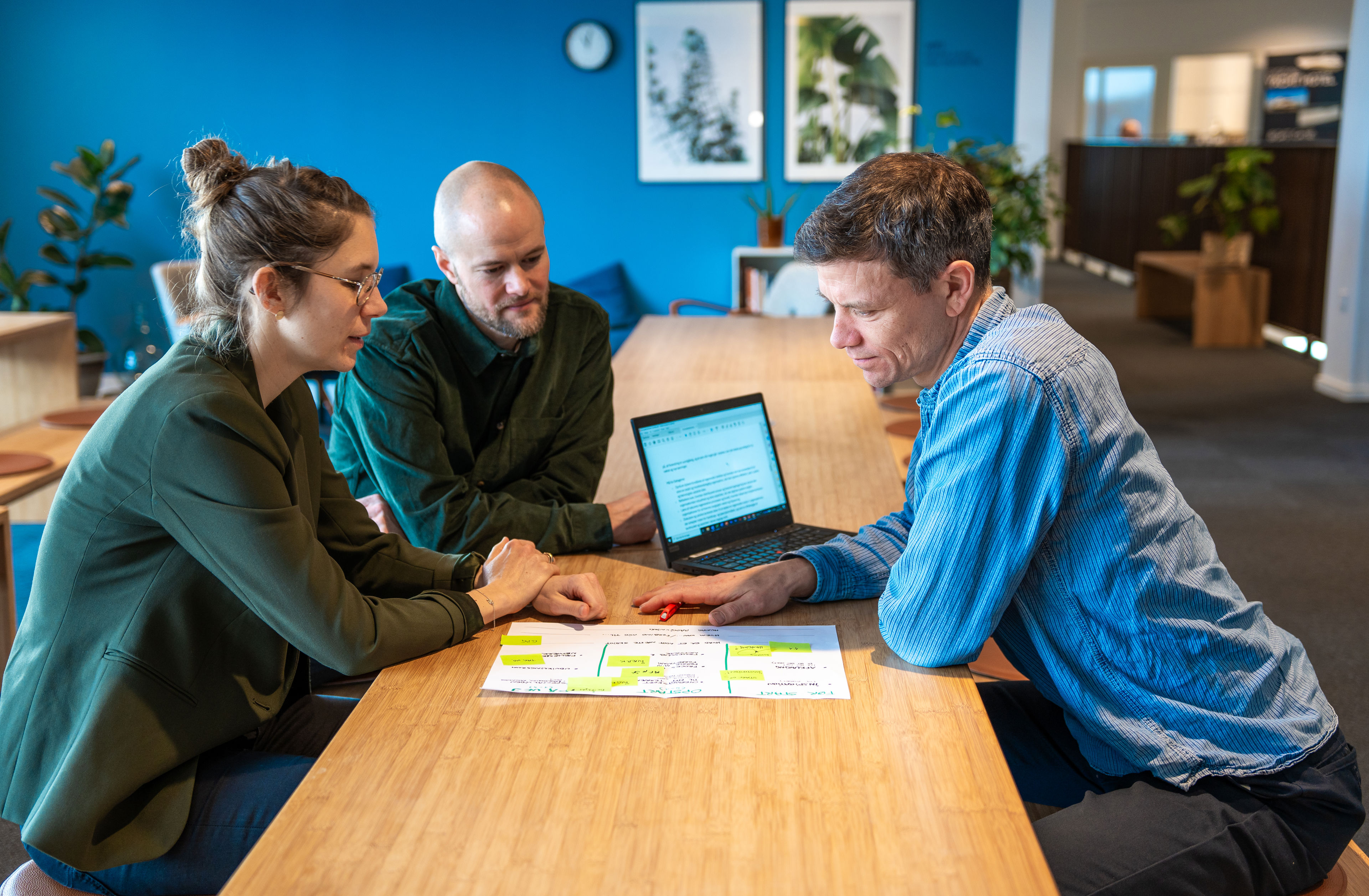Tre personer der sidder ved et bord med en computer