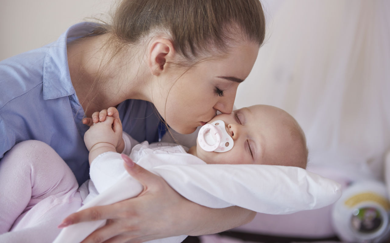 Kvinde kysser baby, med sut i munden, på kinden