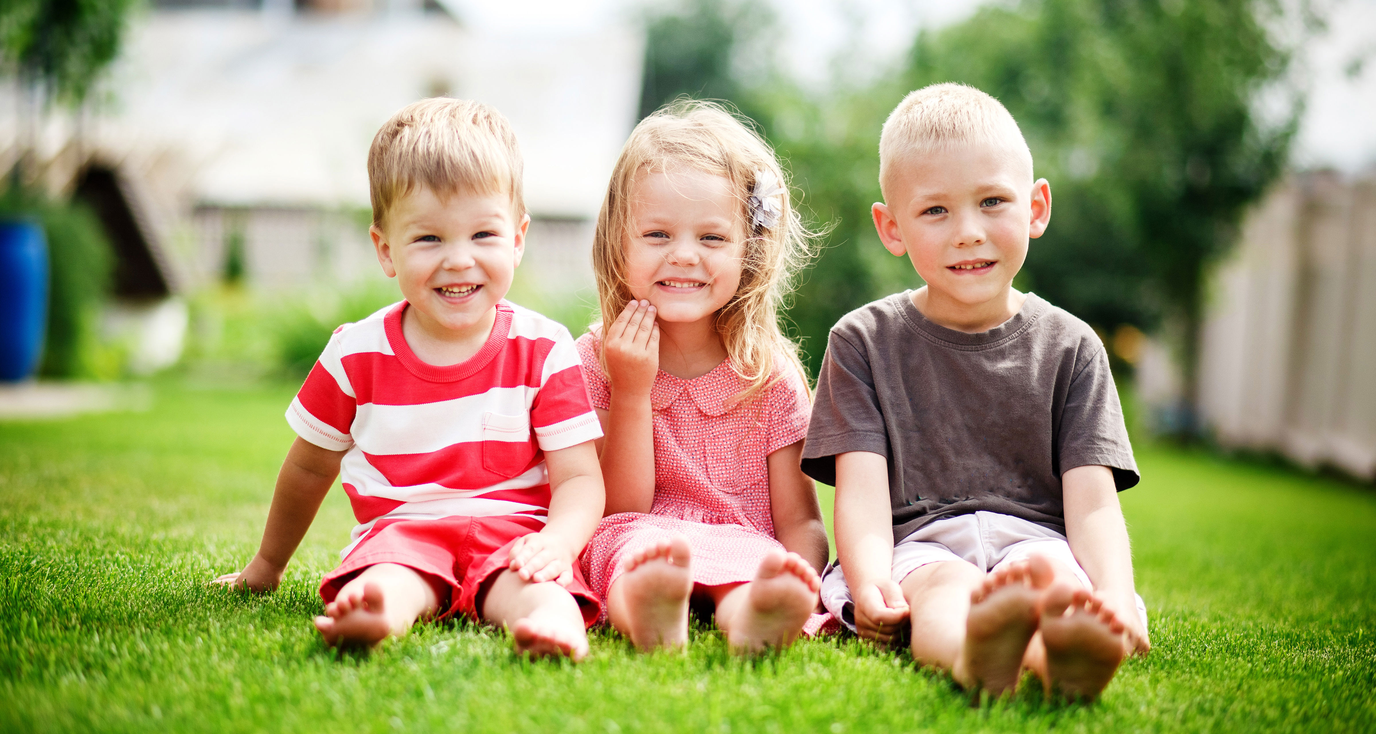 Tre mindre børn sidder på græsset ved siden af hinanden