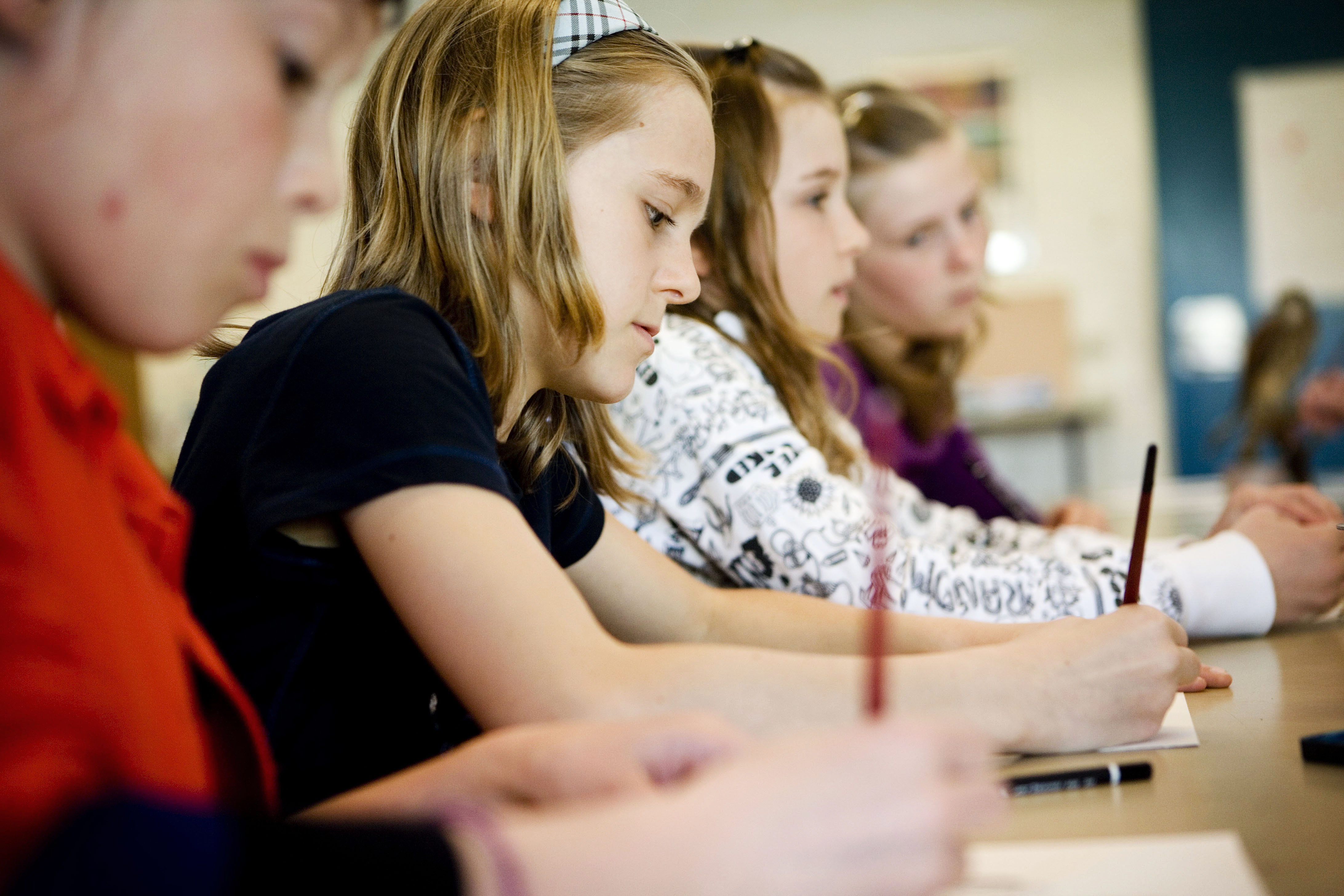 Fire skolelever sidder og skriver med hver deres blyant på et stykke papir.