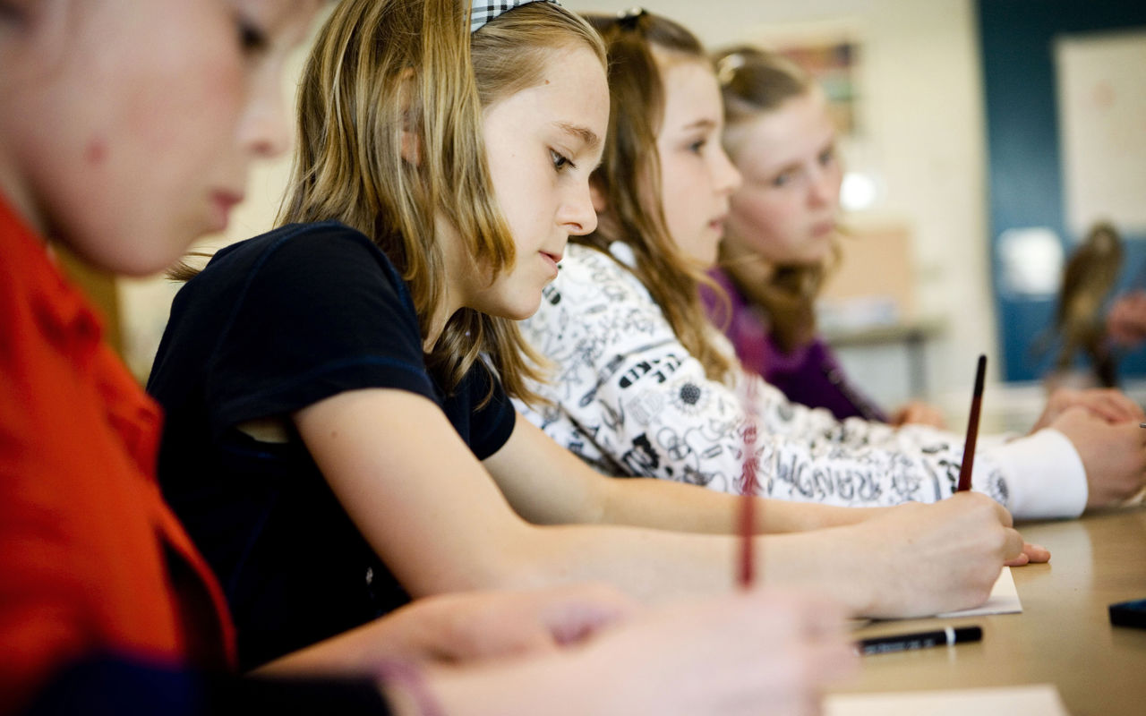 Fire skolelever sidder og skriver med hver deres blyant på et stykke papir.