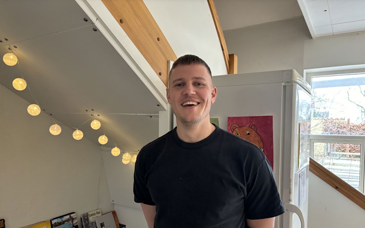 Ung smilende mand stående foran køleskab og bøger