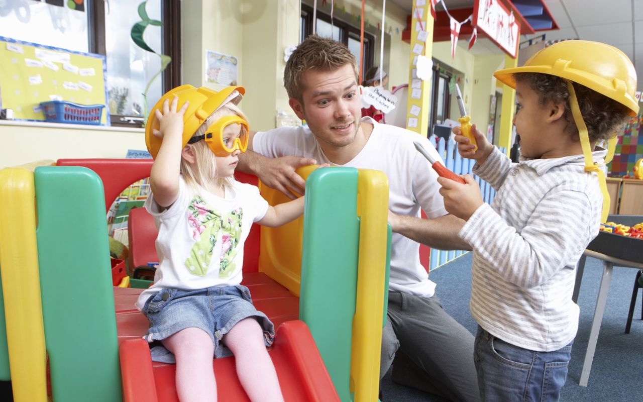 To børn som leger sammen med en mandlig pædagog